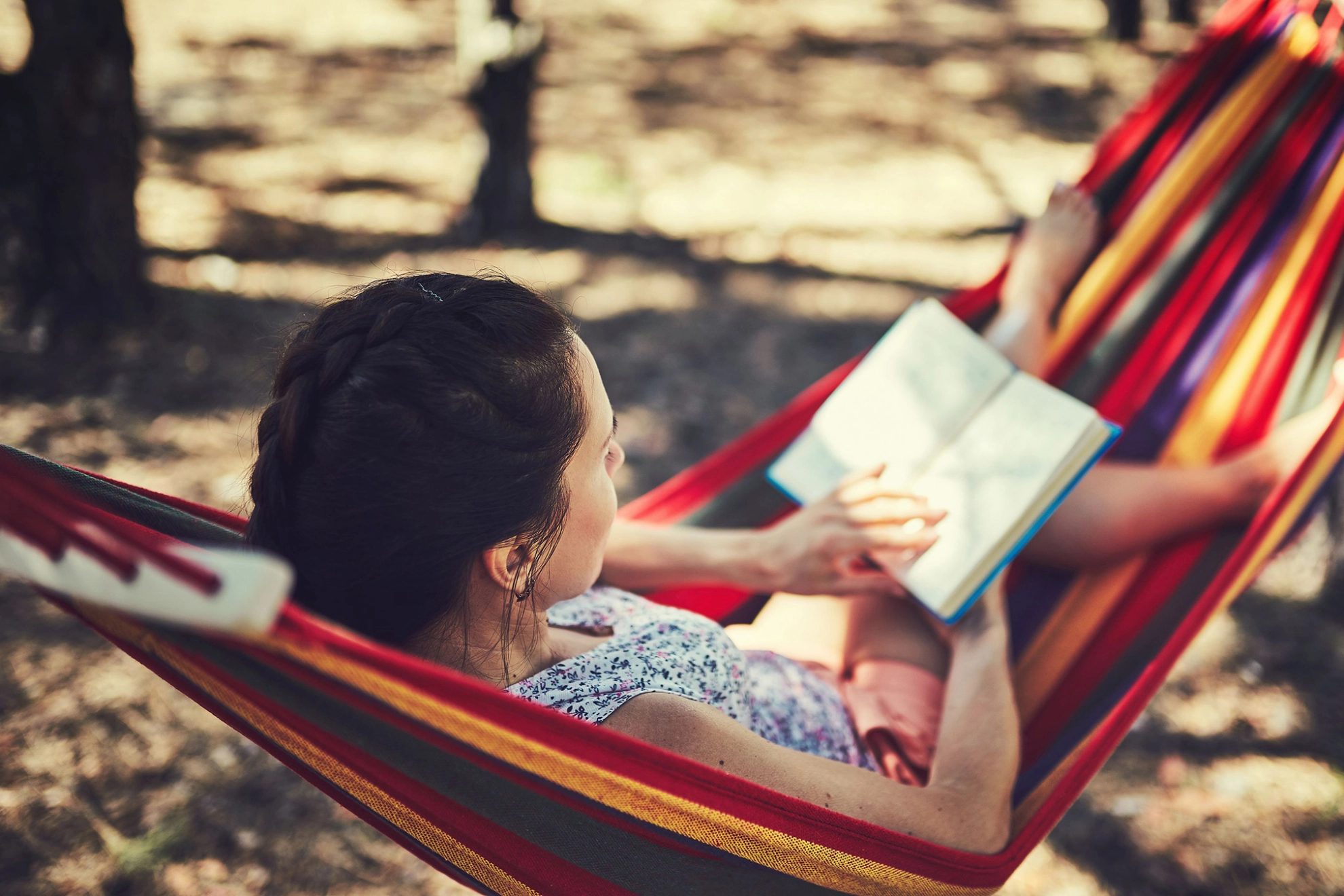 Junge Frau liegt in einer Hängematte und liest ein Buch