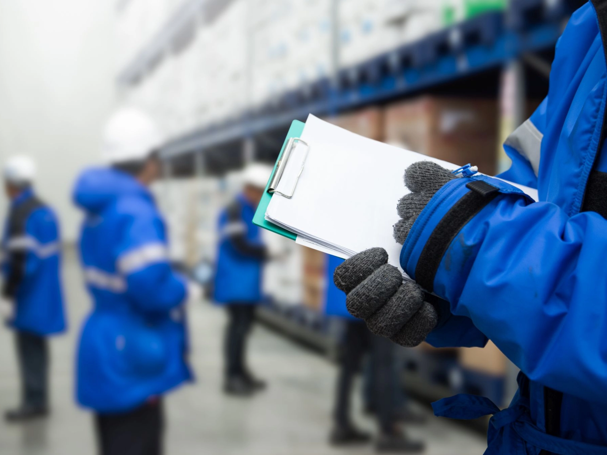 ein Beschäftiger prüft Lagerware in einem Kühlraum, im Hintergrund weitere Kolleginnen und Kollegen