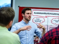 Junger Mann steht vor Flipchart und erklärt etwas.