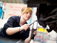 Auszubildende KFZ-Mechanikerin repariert ein Auto.
